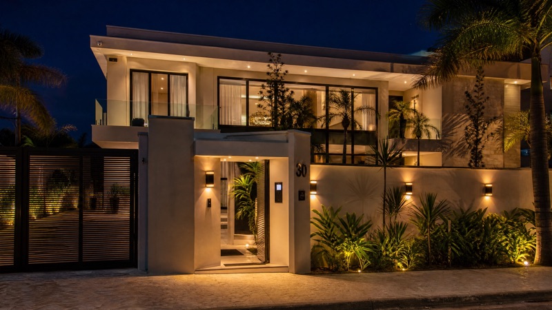 Casa de alto padrão à noite com iluminação inteligente, portão automatizado e câmeras de segurança KiWi